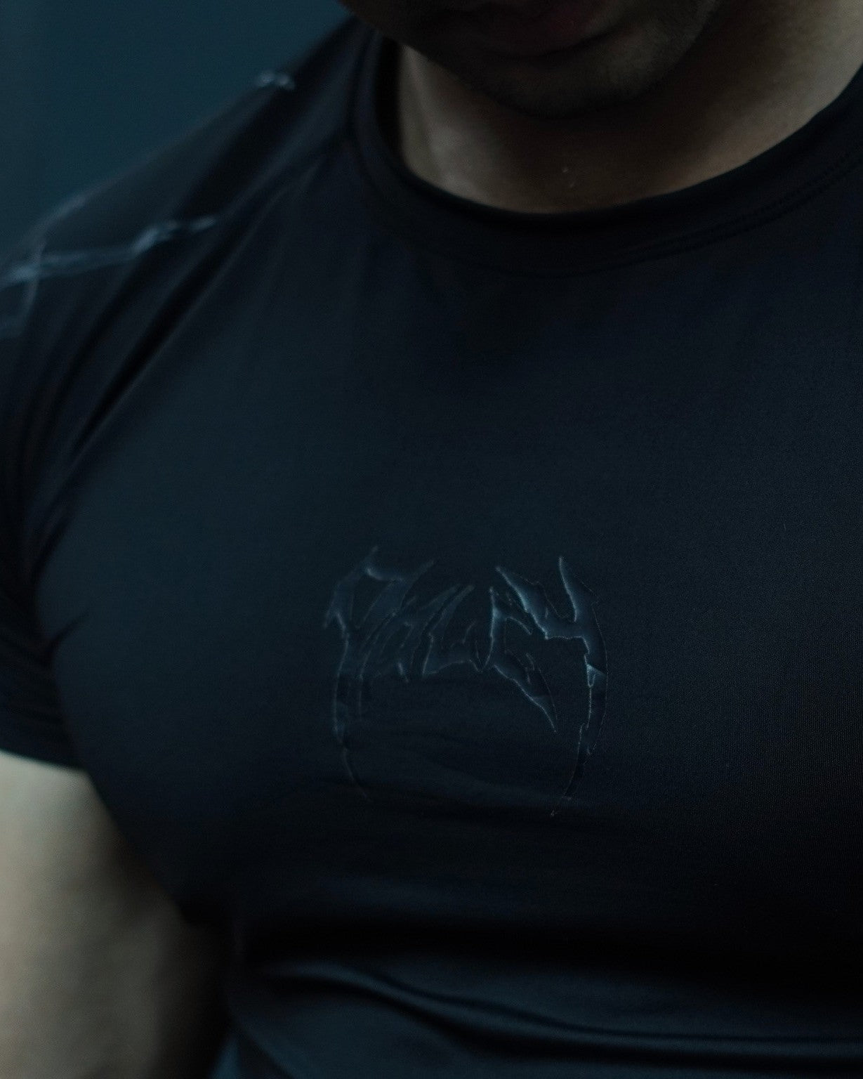 Black t-shirt with a logo on the chest against a dark background